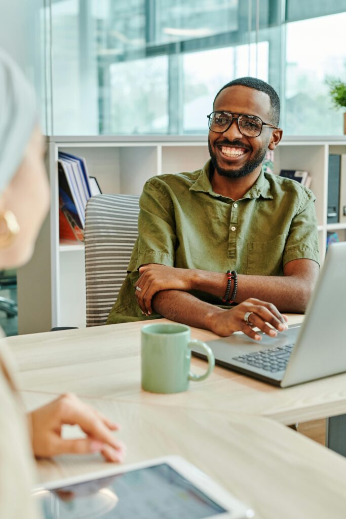 pexels-photo-8068257-8068257 Cheerful man working at a desk in a modern office with laptop and coffee mug.